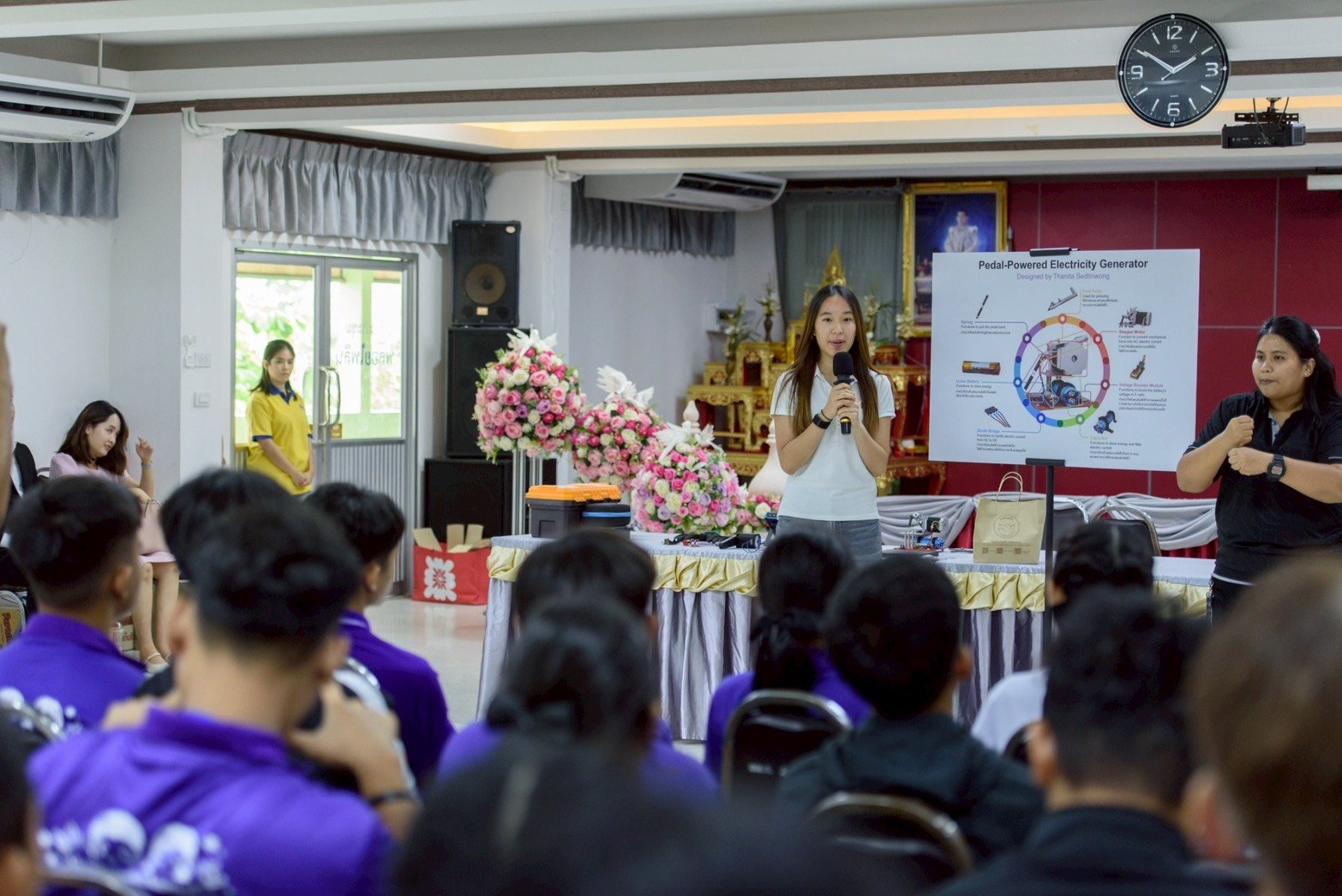 Winnie presenting her pedal-powered electricity generator, with a sign language interpreter